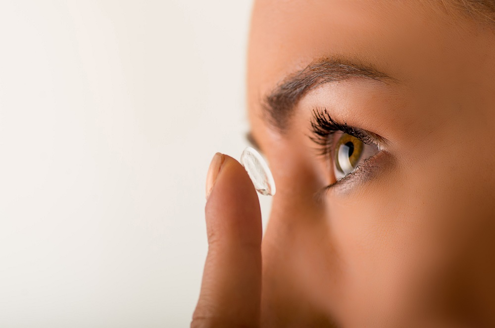 Close up of a young woman putting contact lens in her eye close up.