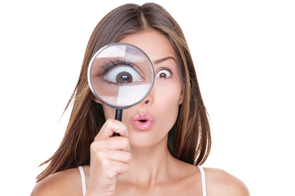 Funny expression. Shocked woman looking through a magnifying gla