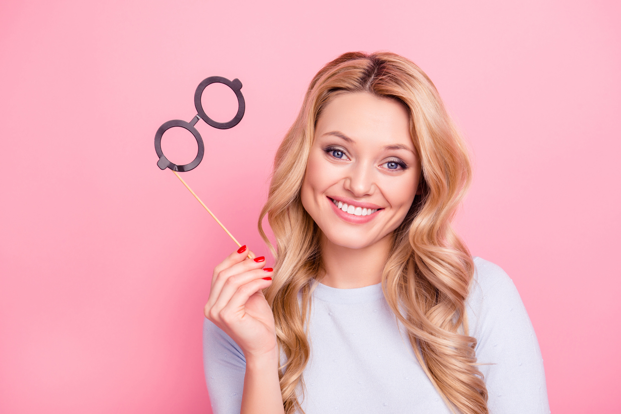 Young woman on pink background removing fake glasses