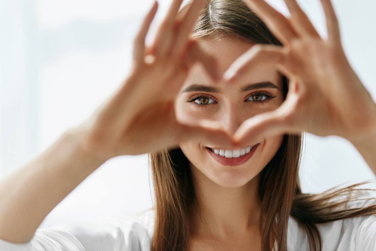 Woman looking through heart-shape she made with hands representing love of clear lasik vision.